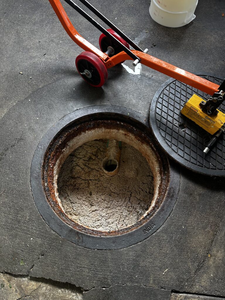Open grease interceptor with visible baffle tee needing repair